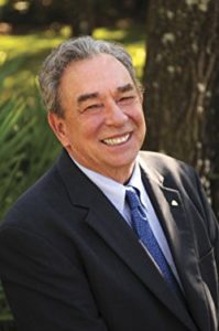 R C Sproul smiling in a black coat and a blue tie